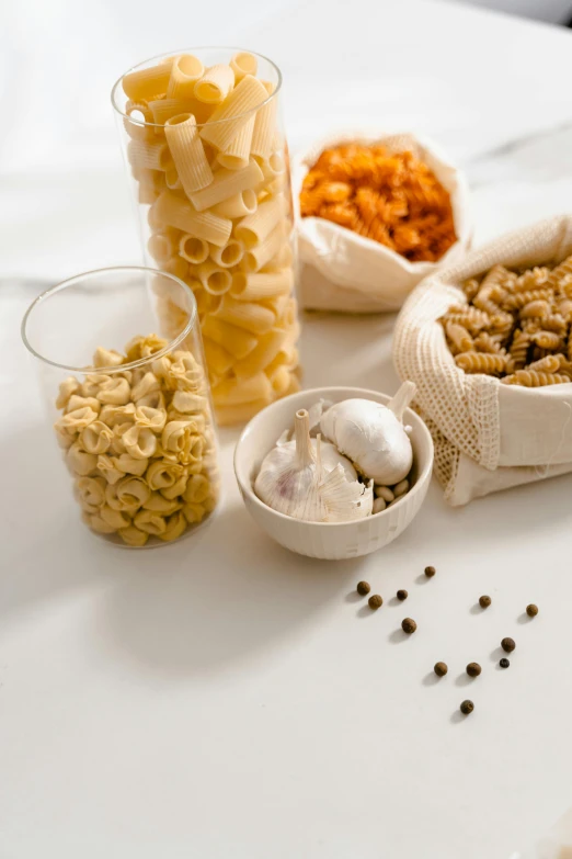 a white table topped with bowls of food, pasta, detailed product image, jars, petite