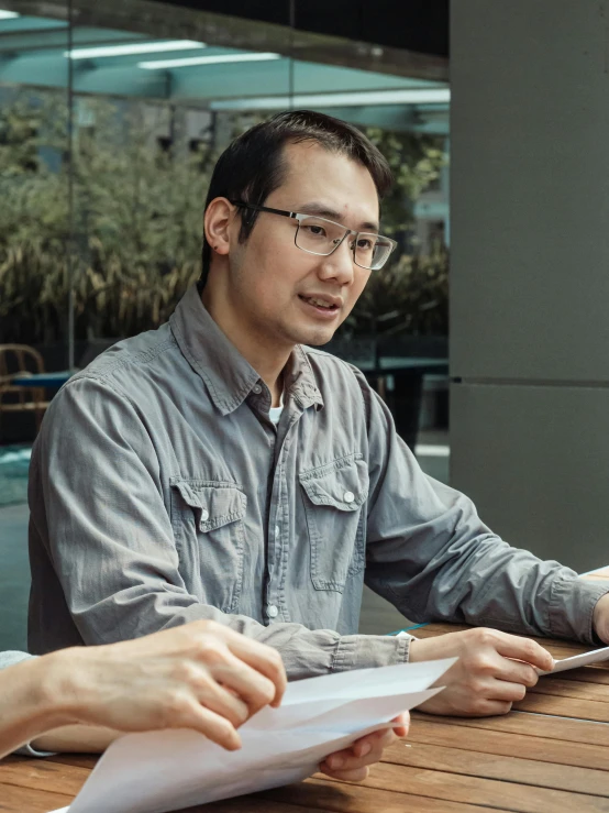 a couple of people that are sitting at a table, inspired by Fei Danxu, pexels contest winner, realism, man with glasses, asian male, profile image, sitting on a mocha-colored table