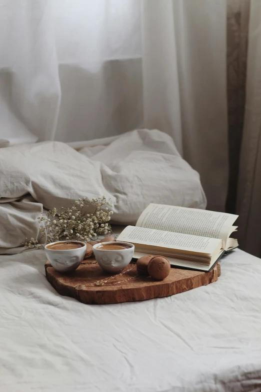 an open book sitting on top of a bed next to a cup of coffee, a still life, pexels contest winner, romanticism, wood cups, gif, snacks, brown and white color scheme