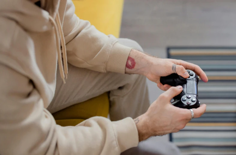 a man sitting on a couch holding a video game controller, trending on pexels, photograph of a sleeve tattoo, sitting on a red button, valorant game style, ps 4