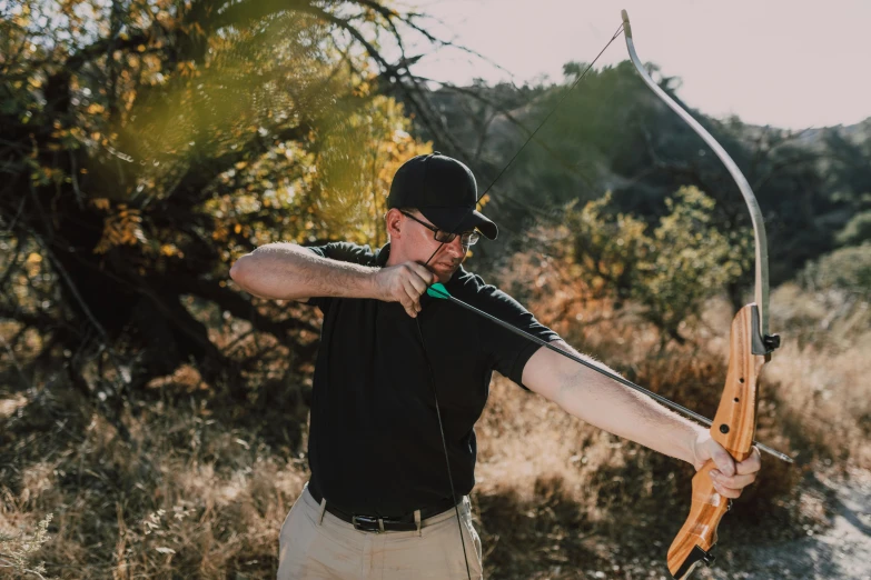 a man standing in a field holding a bow and arrow, a portrait, unsplash, avatar image, professional gunsmithing, new mexico, behind the scenes photo