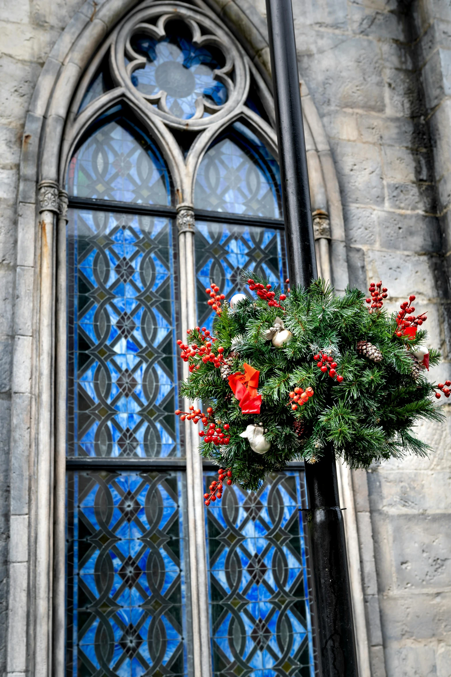 a church window with a wreath hanging from it's side, a photo, inspired by Master of Saint Giles, trending on unsplash, holiday season, square, gleaming silver and rich colors, tall spires