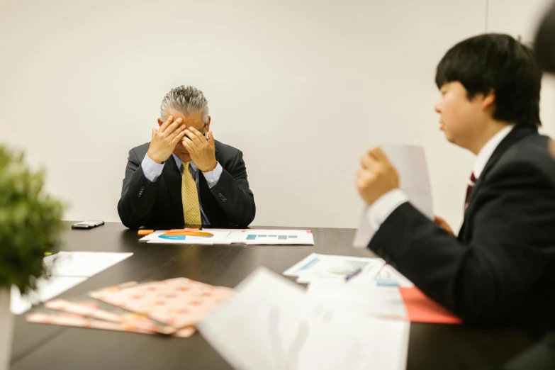 a man sitting at a table covering his face with his hands, shin hanga, business meeting, joongwon jeong, thumbnail, disappointed