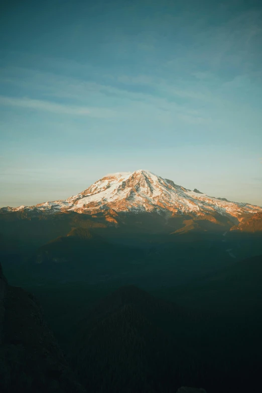 a mountain with a snow covered peak in the distance, in the golden hour, a high angle shot, volcano, clear skies