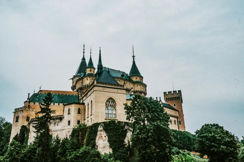 a castle sitting on top of a lush green hillside, a photo, by Emma Andijewska, pexels contest winner, art nouveau, black domes and spires, castelvania, front side, bl