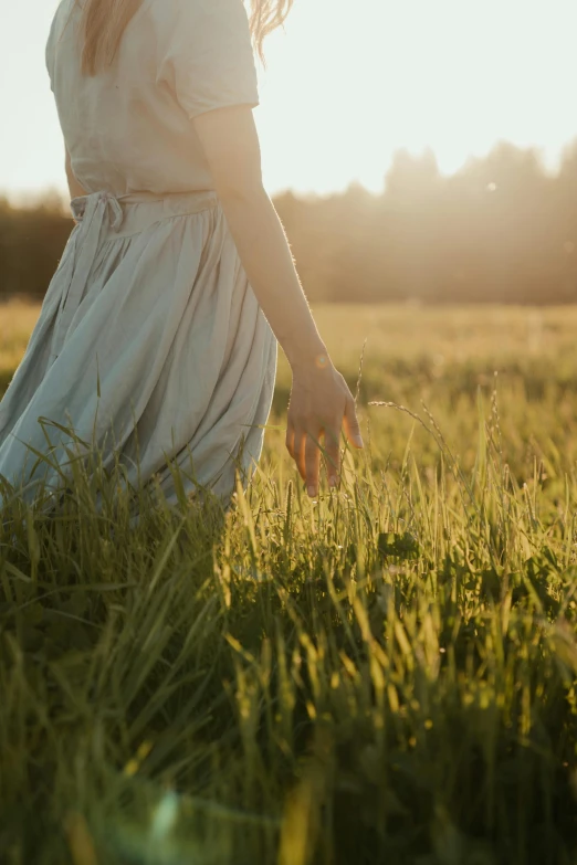 a woman walking through a field at sunset, unsplash, romanticism, soft green natural light, sundress, lightly dressed, grass