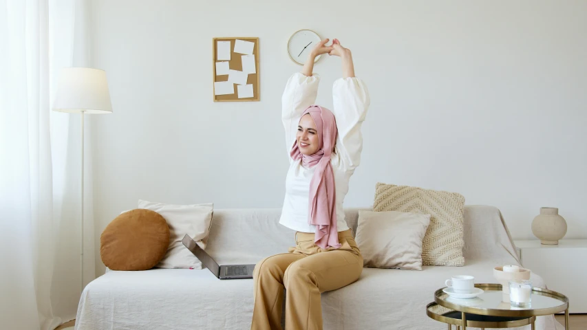 a woman sitting on top of a couch holding a frisbee, inspired by Maryam Hashemi, trending on pexels, arabesque, white hijab, clock, pose(arms up + happy), brown and pink color scheme