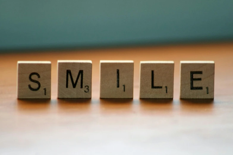a wooden block with the word smile written on it, a picture, by Emma Andijewska, pexels, letterism, uniform teeth, building blocks, profile pic, cubes on table