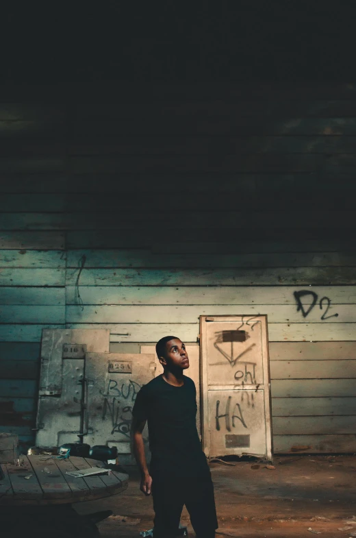 a man standing in a dark room with graffiti on the walls, an album cover, pexels contest winner, plain background, taken at golden hour, ( ( theatrical ) ), dark warehouse