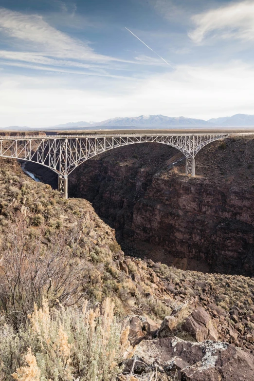 a bridge over a canyon with mountains in the background, white sweeping arches, high above the ground, overhead, overlooking