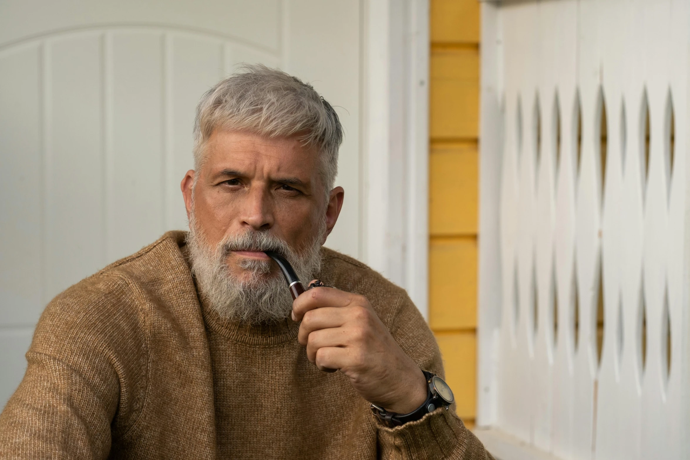 a man sitting at a table with a pipe in his mouth, inspired by László Beszédes, trending on pexels, grey trimmed beard, standing outside a house, he is wearing a brown sweater, professional image