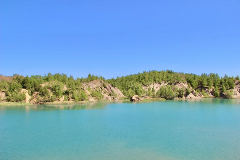 a large body of water surrounded by trees, by Yerkaland, les nabis, rock quarry location, sky blue, teal energy, pine forests