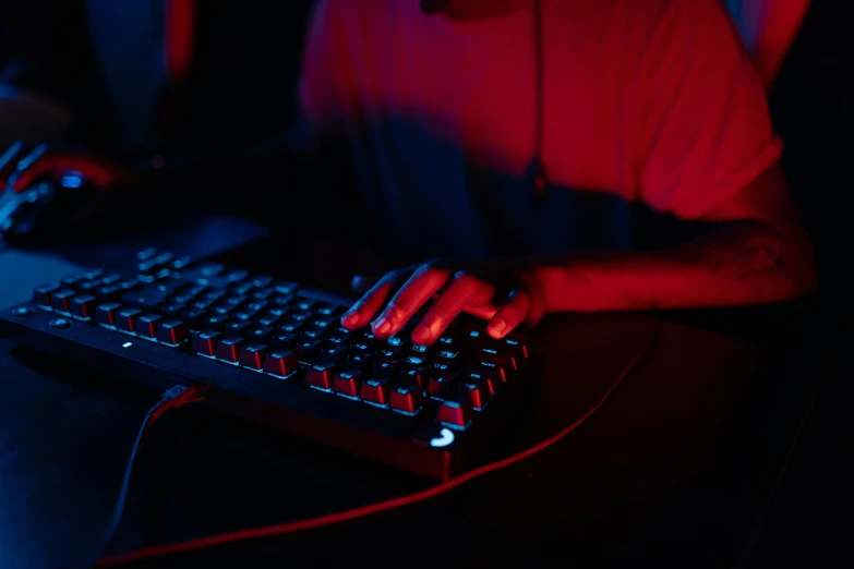 a man sitting in front of a computer keyboard, red and obsidian neon, bottom angle, shot on sony a 7, holding controller