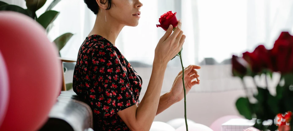 a woman holding a flower in front of a bunch of balloons, by Julia Pishtar, pexels contest winner, romanticism, holding a red rose, oona chaplin, close up to a skinny, woman with black hair