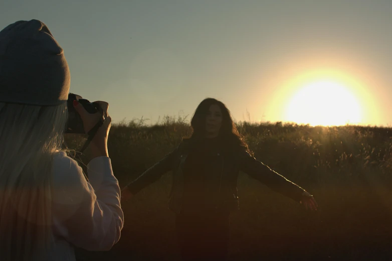 a woman taking a picture of another woman in a field, a picture, by Attila Meszlenyi, unsplash, video art, sun down, production still, film still promotional image, low - angle shot