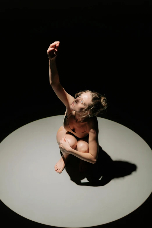 a woman sitting on top of a white circle, by Grace Polit, crying and reaching with her arm, soft lighting from above, sydney hanson, looking towards camera