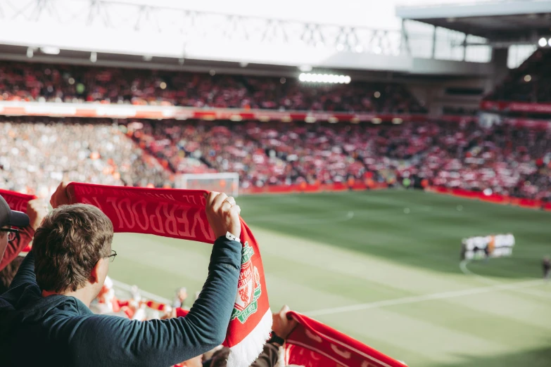 a man holding up a scarf at a soccer game, by Julia Pishtar, pexels contest winner, liverpool football club, overlooking, thumbnail, fanbox