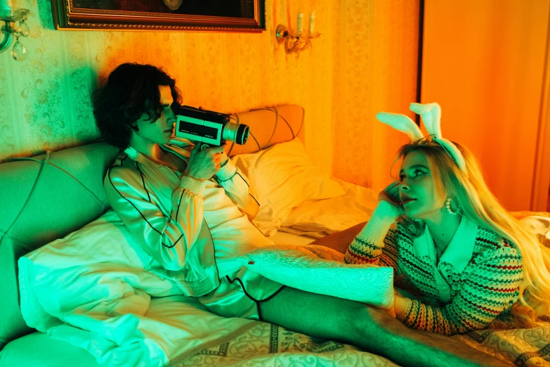 a couple of women sitting on top of a bed, inspired by Nan Goldin, pexels contest winner, pop art, orange and cyan lighting, camcorder, emma watson in bed, joe keery