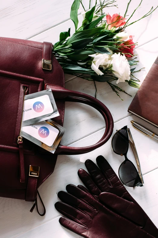 a purse sitting on top of a table next to a bunch of flowers, pair of keycards on table, maroon, in suitcase, vp of marketing