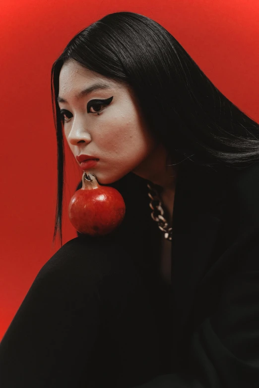 a woman sitting down with an apple in her hand, an album cover, inspired by Taro Yamamoto, trending on pexels, jingna zhang, pomegranate, mall goth, irelia