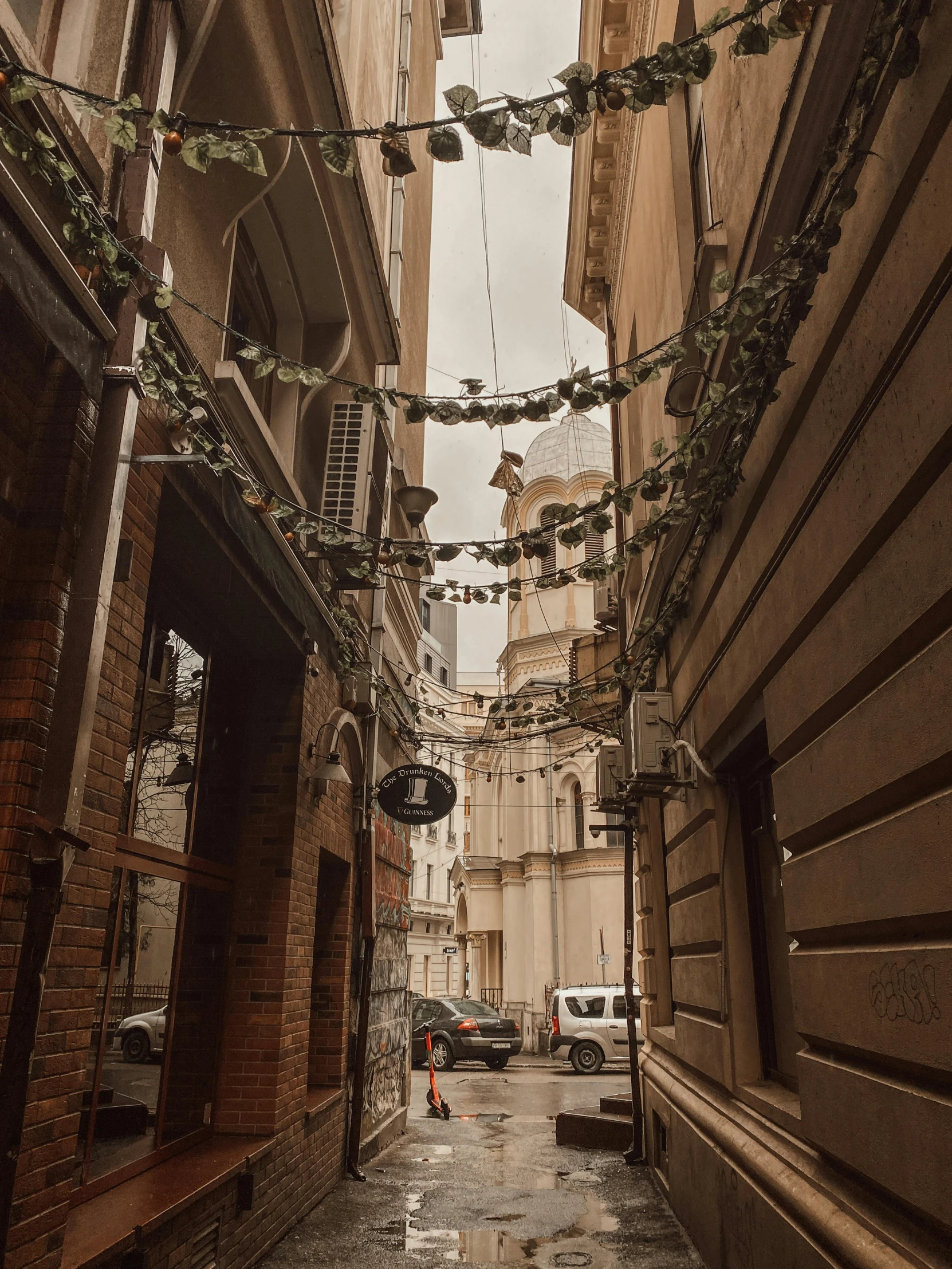 a narrow alley with a clock tower in the background, by Emma Andijewska, pexels contest winner, lots of hanging cables and wires, young handsome pale roma, 🤬 🤮 💕 🎀, grey skies rain