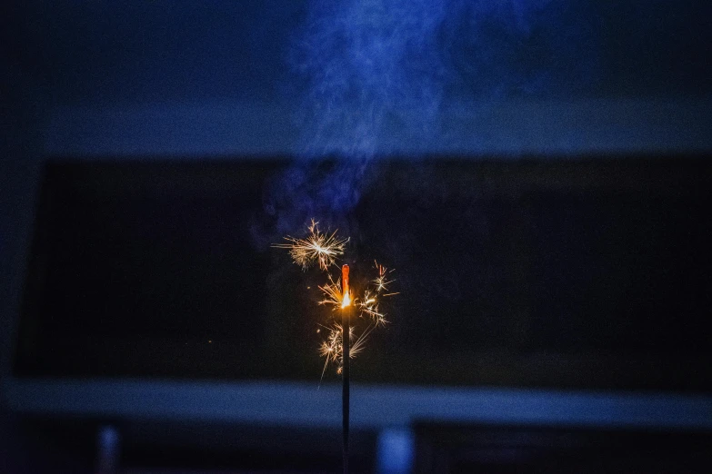 a sparkler is lit up in the dark, blue smoke, fireworks in the background, tiny firespitter, red smoke coming from lamp