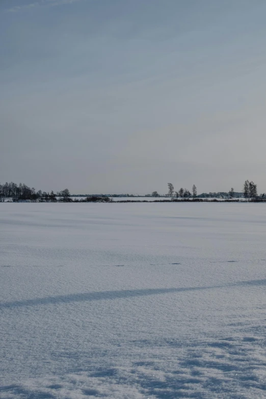 a man riding a snowboard across a snow covered field, by Daarken, land art, viewed from afar, helmond, farm land, grey