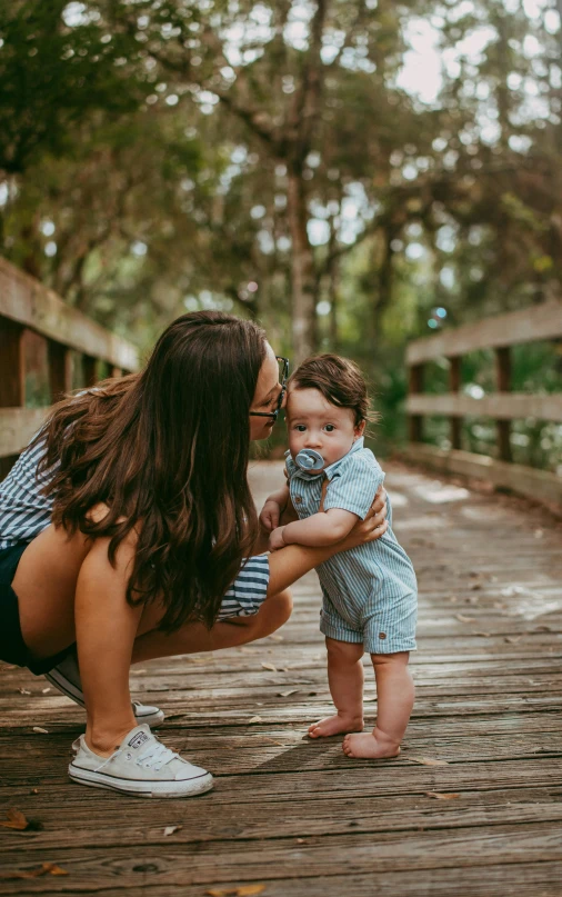 a woman holding a baby on a wooden bridge, by Matt Cavotta, pexels contest winner, hispanic, cheeks, avatar image, son