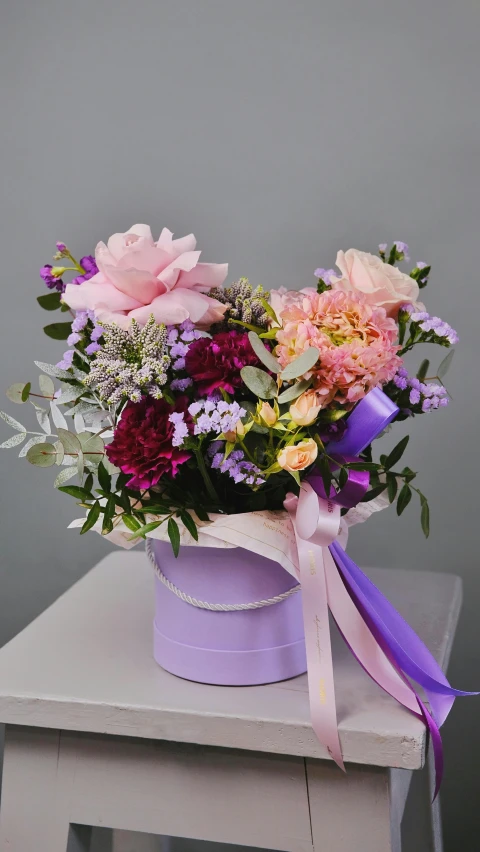 a bucket filled with flowers sitting on top of a table, a pastel, inspired by Eden Box, pexels, purple ribbons, elegantly dressed, angle view, various colors