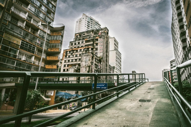 a man riding a skateboard down a street next to tall buildings, an album cover, inspired by Elsa Bleda, unsplash, brutalism, sky bridge, buenos aires, building crumbling, an abandoned old