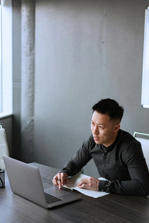a man sitting at a table working on a laptop, inspired by Fei Danxu, pexels contest winner, wearing business casual dress, half asian, grey, pondering