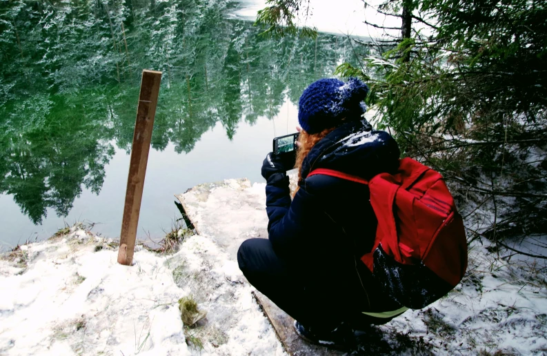 a person taking a picture of a body of water, in a snowy forest setting, planning, technical, mountain water