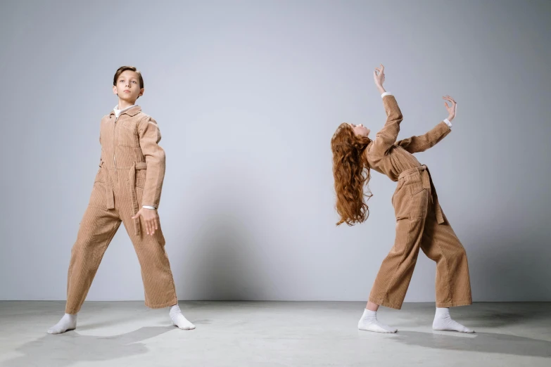 a couple of people standing next to each other, inspired by Vanessa Beecroft, trending on pexels, kawaii playful pose of a dancer, air force jumpsuit, brown, 15081959 21121991 01012000 4k