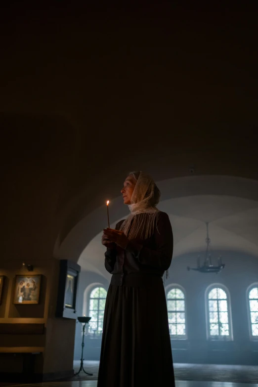 a woman holding a lit candle in a dark room, a picture, inspired by Andrei Rublev, unsplash, in this church interior, high quality photo, historical reenactment, #oc