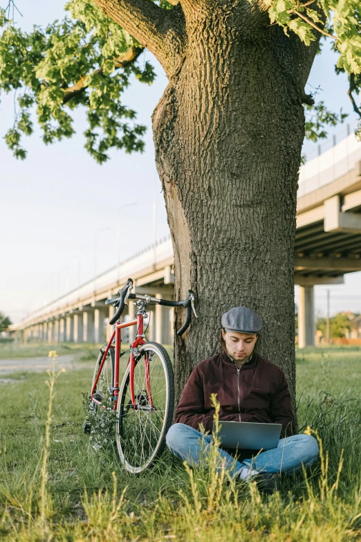 a man sitting under a tree with a laptop, by Carey Morris, bicycles, bridges, rex orange county, raphael personnaz