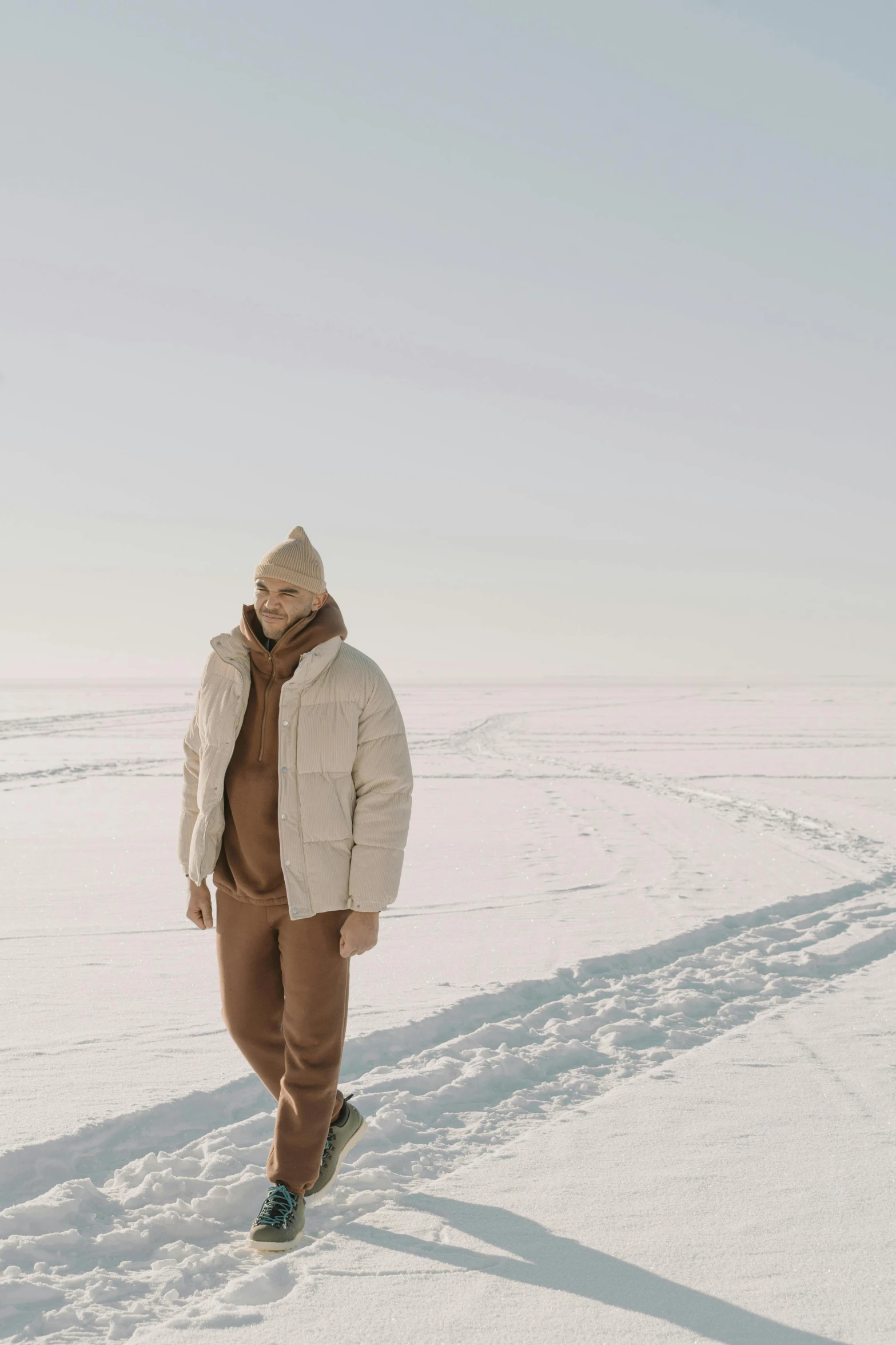 a man walking across a snow covered field, inspired by Louisa Matthíasdóttir, trending on pexels, beige hoodie, wearing a track suit, model posing, inuit