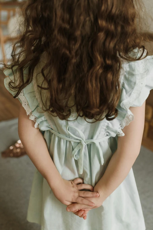 a little girl standing in a room with her hands on her hips, a picture, inspired by Elsa Beskow, pexels, soft blues and greens, detail shot, hands in her hair. side-view, full product shot