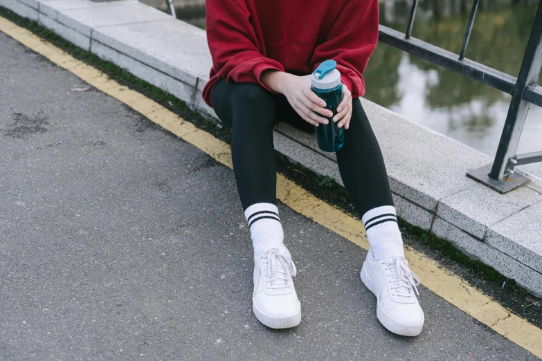 a woman sitting on a ledge next to a body of water, trending on pexels, graffiti, water bottles, white tights, sneaker photo, girl wearing uniform