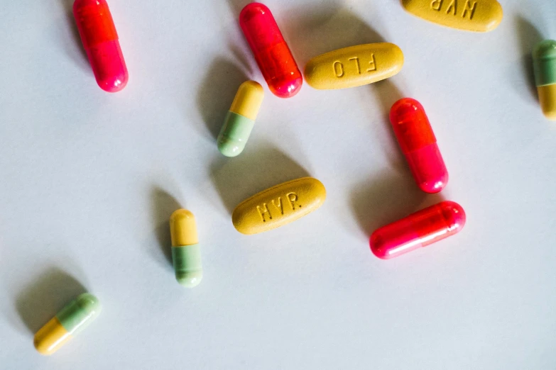 a bunch of pills sitting on top of a table, yellow and red, jen atkin, uhq, on a white table