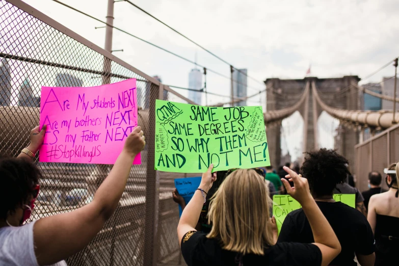 a group of people holding up signs in front of a fence, by Whitney Sherman, pexels, feminist art, pewdiepie selfie at a bridge, new york city, 9/11, polychromatic