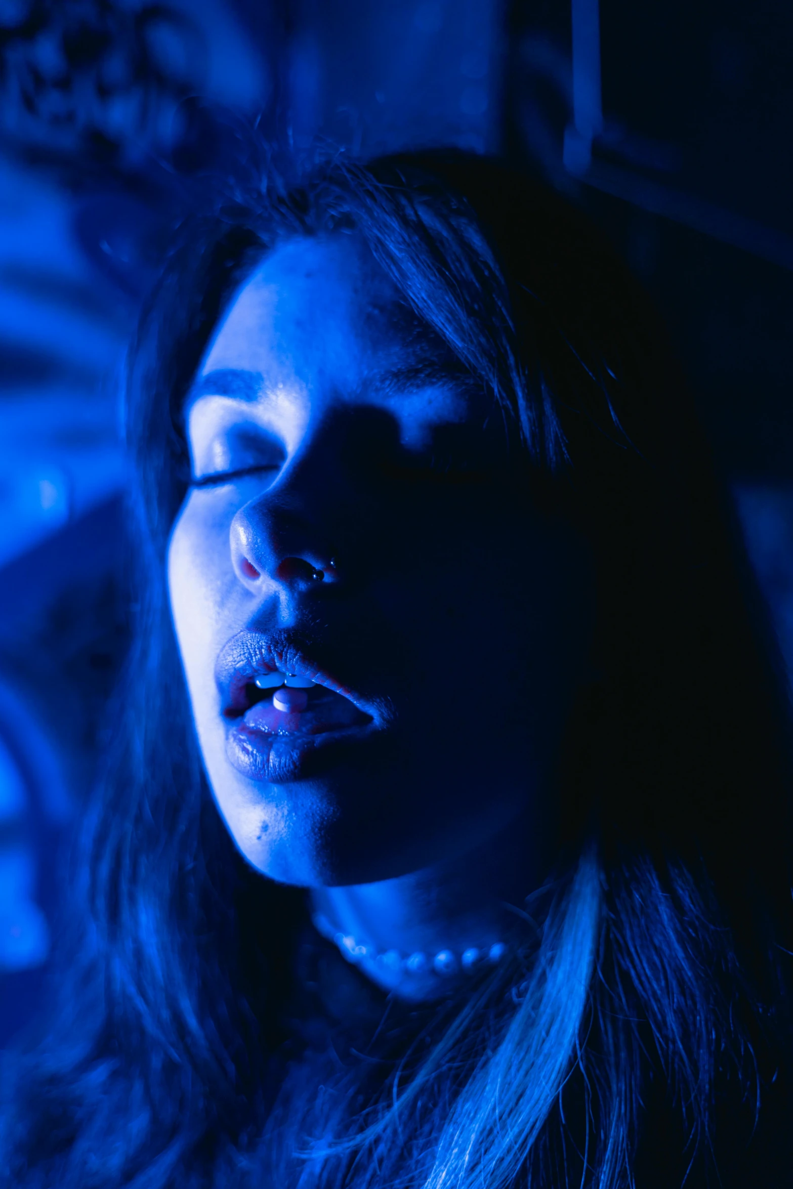 a woman with her eyes closed in a dark room, inspired by Elsa Bleda, reddit, bursting with blue light, septum piercing, still from a music video, thick lips