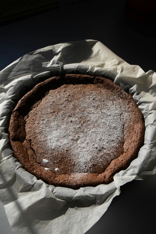 a chocolate cake sitting on top of a piece of paper, inspired by Gentile Bellini, covered in white flour, rim lit, 3/4 view from below, circle pit