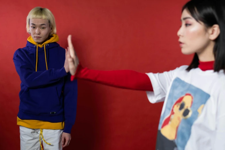 two women standing next to each other in front of a red wall, inspired by Satoshi Kon, trending on pexels, dabbing, in blue and yellow clothes, cai xukun, bullying