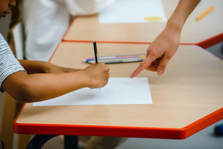 a close up of a person writing on a piece of paper, a child's drawing, by Matthias Stom, pexels contest winner, academic art, back of hand on the table, radial symmetry, standing in class, lachlan bailey