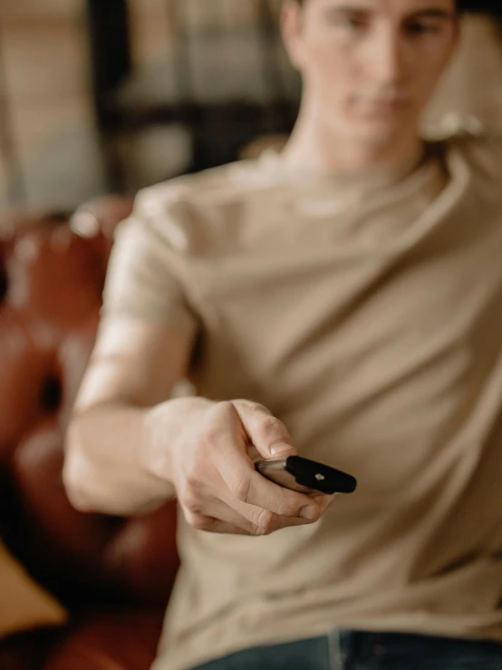 a man sitting on a couch holding a remote control, by Adam Marczyński, trending on pexels, happening, shungite bangle, avatar image, holding hk pistol in hand, thin young male