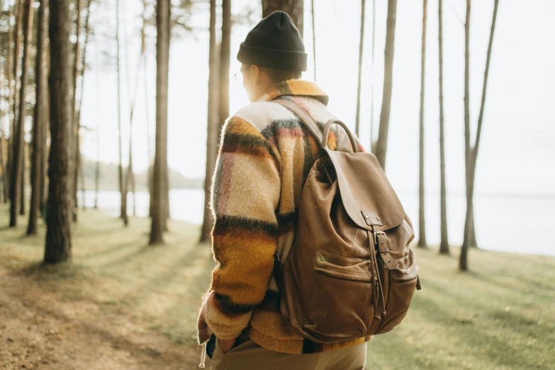 a person walking in the woods with a backpack, by Carey Morris, trending on pexels, wearing a brown leather coat, laid back features, thumbnail, background image