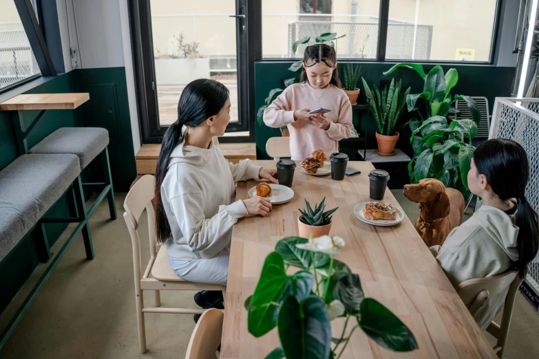 a group of people sitting around a wooden table, with a kid, big interior plants, profile image, breakfast