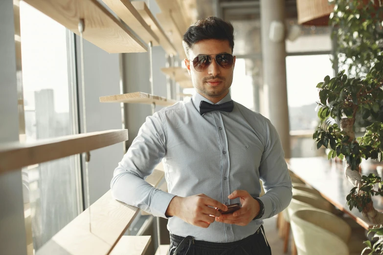 a man in a bow tie looking at his cell phone, pexels contest winner, open shirt, middle eastern, elegant confident pose, sunglasses on