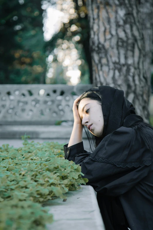 a woman sitting on a bench next to a tree, an album cover, unsplash, realism, wearing a dark hood, sleepy expression, asian women, 15081959 21121991 01012000 4k