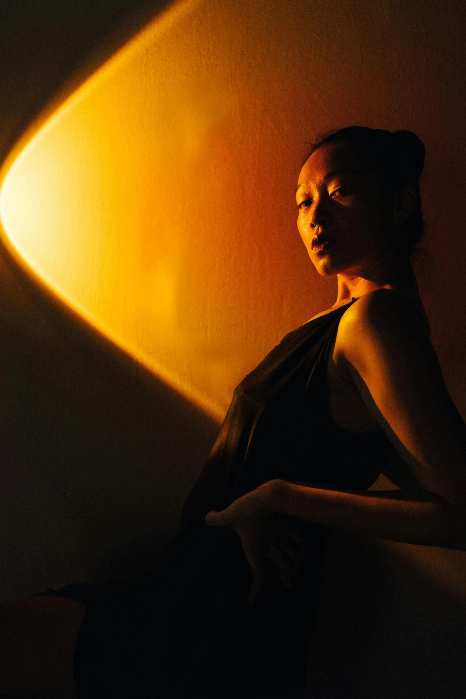 a woman sitting in a dimly lit room, light and space, asian sun, jeffrey jones dynamic lighting, promo image, ambient amber light